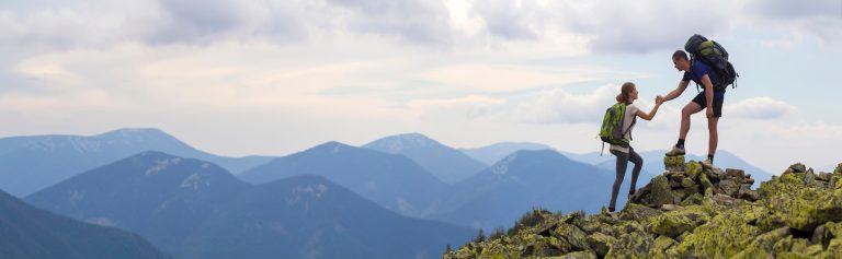 Two mountain climbers helping each other up the cliff, symbolizing successful drug and alcohol treatment in North Carolina.