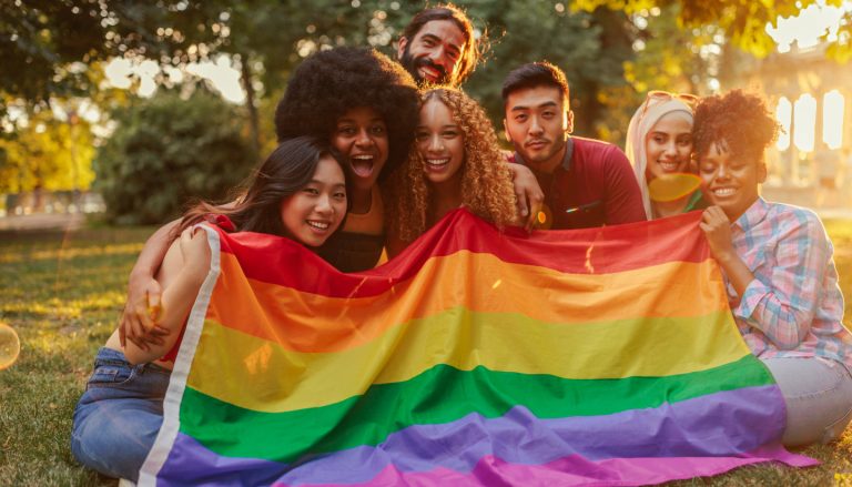 A group of people at sunset holding gay pride flag during pride month.