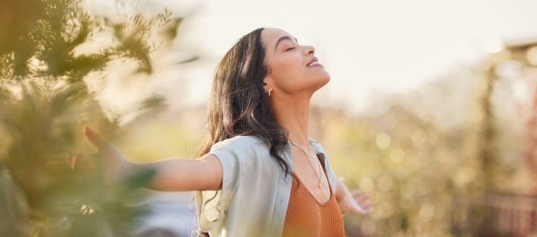 A woman stands outside with her arms outstretched enjoying the fresh air, depicting the joy of addiction recovery.