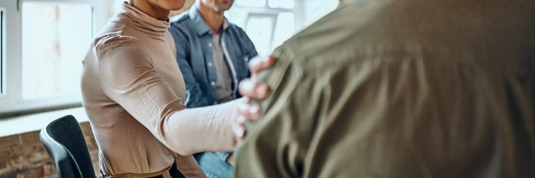 Men and women sitting in a circle during group therapy, supporting each other.